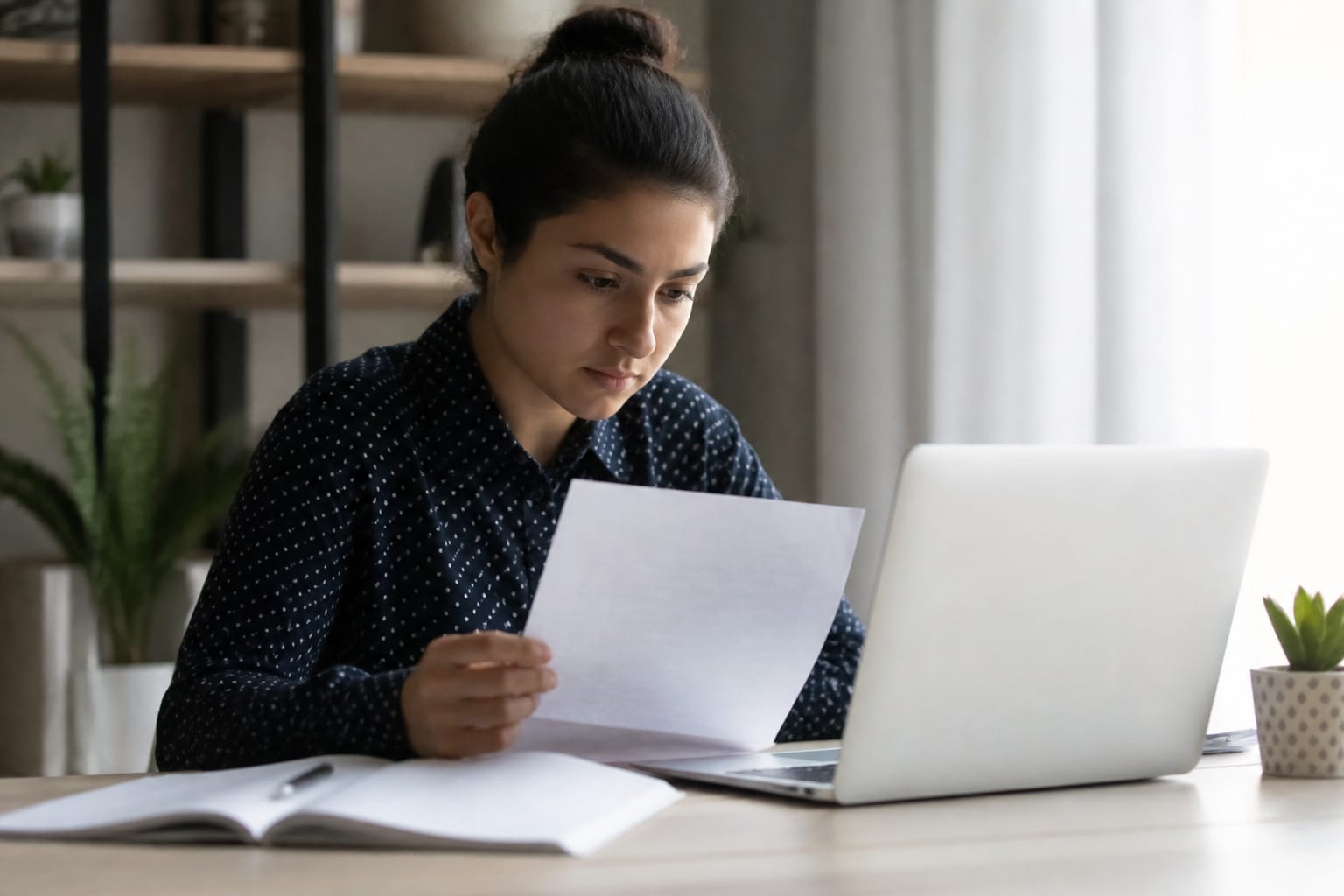 A student reading a printed requirements sheet beside a laptop