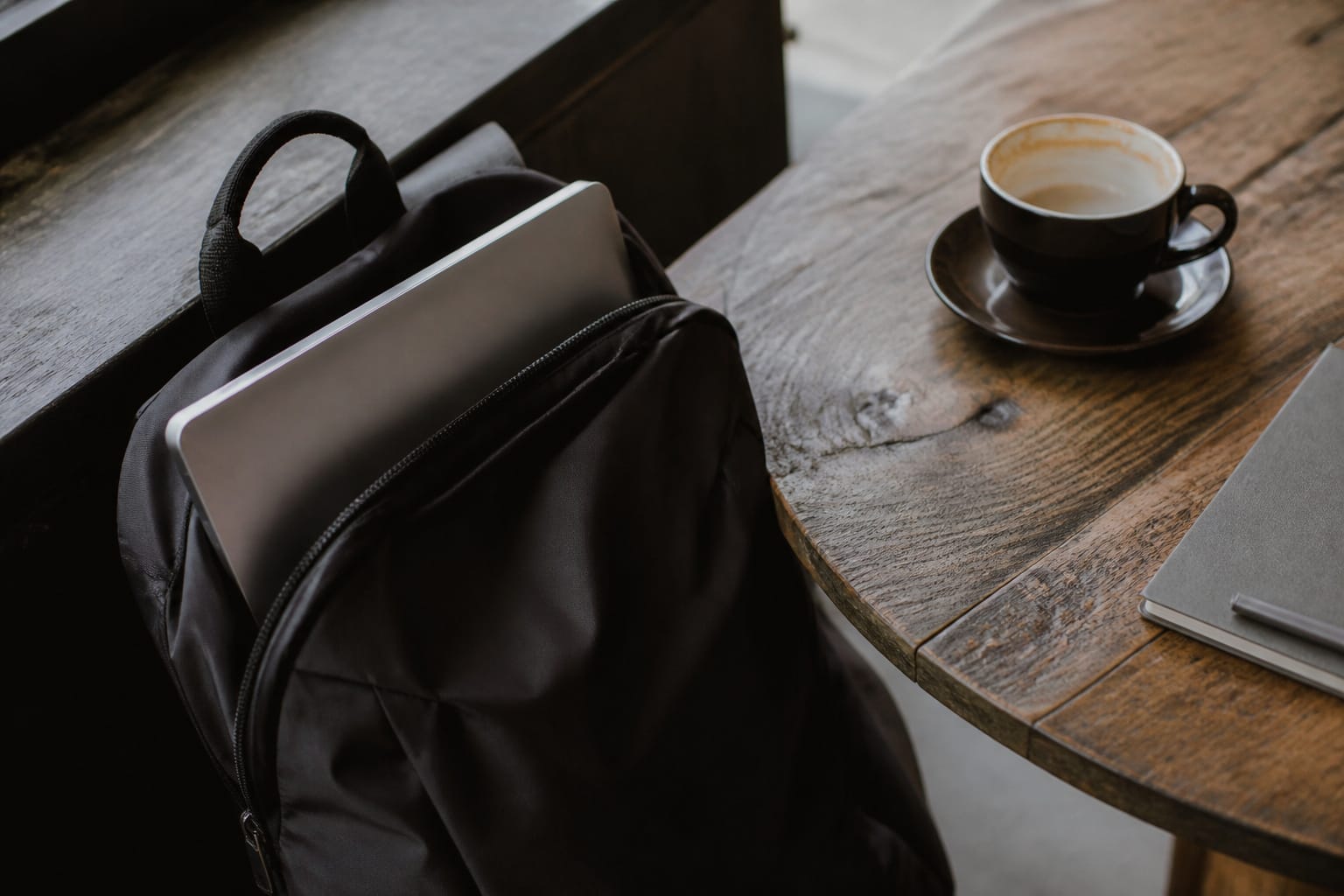 A laptop in a backpack beside a coffee shop table