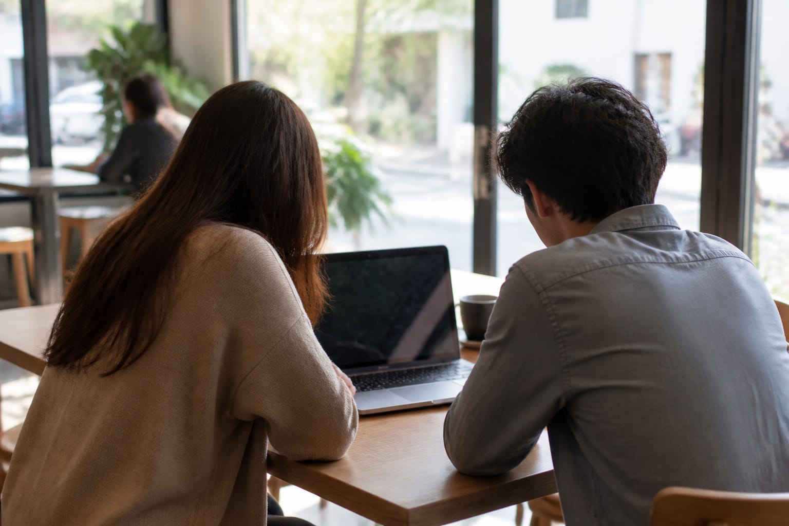 Two people inspecting a laptop at a public cafe table