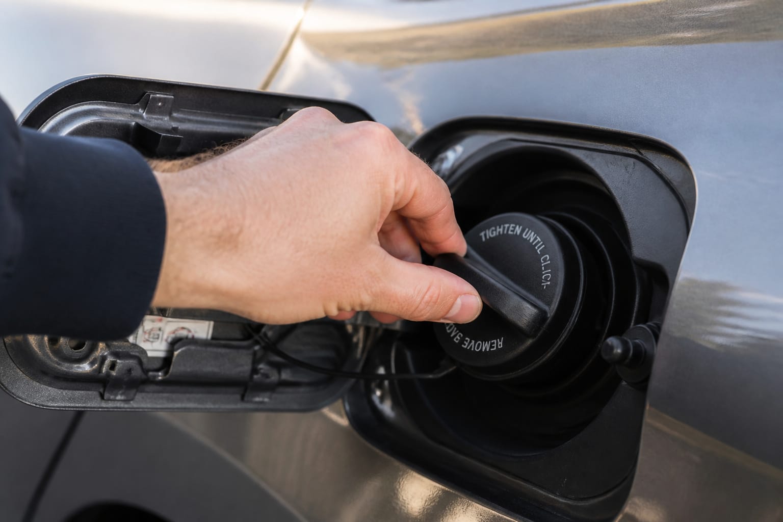 Hand tightening a car's gas cap at the fuel filler door