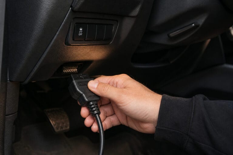 Hand plugging an OBD2 scanner into the port under a car's dashboard