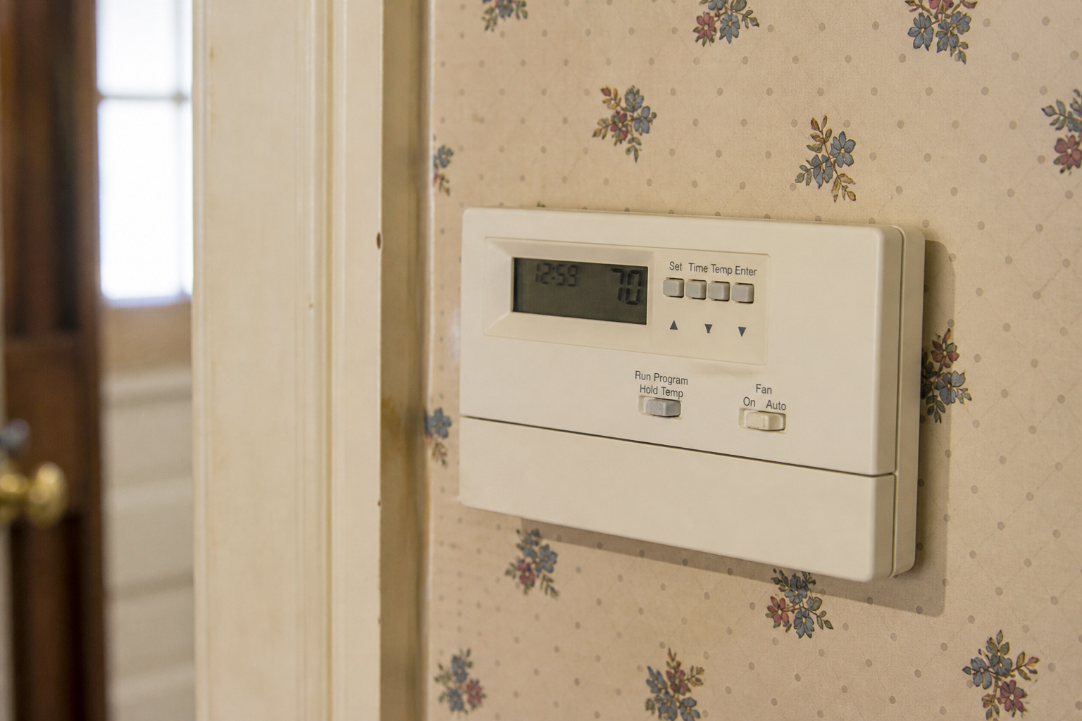 Old programmable thermostat with small buttons mounted on a wall