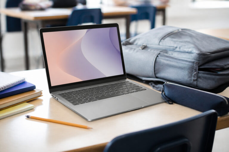 Chromebook-style laptop on a school desk with notebooks and a backpack