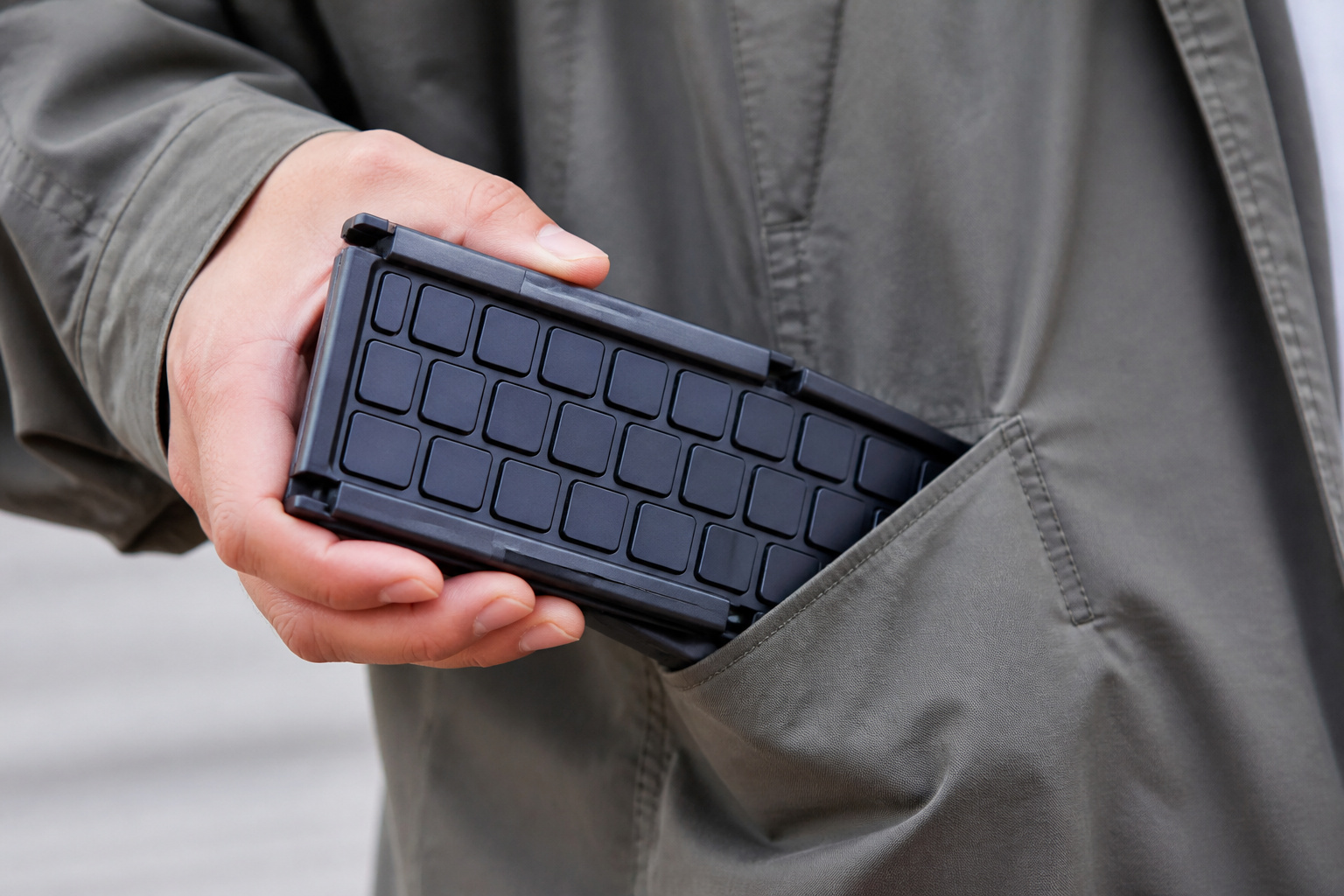 Compact folded keyboard held in a hand next to a jacket pocket