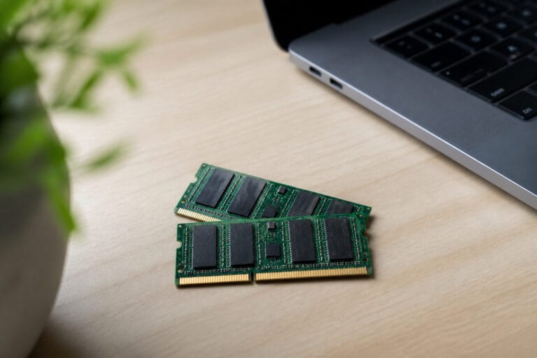 Two memory modules on a clean desk beside a laptop