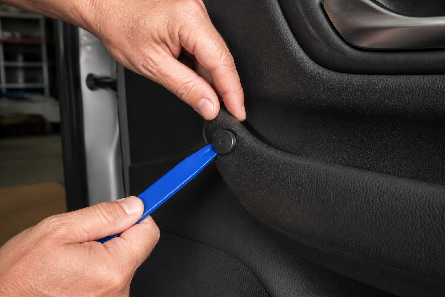 Hands prying a car door panel clip with a trim tool