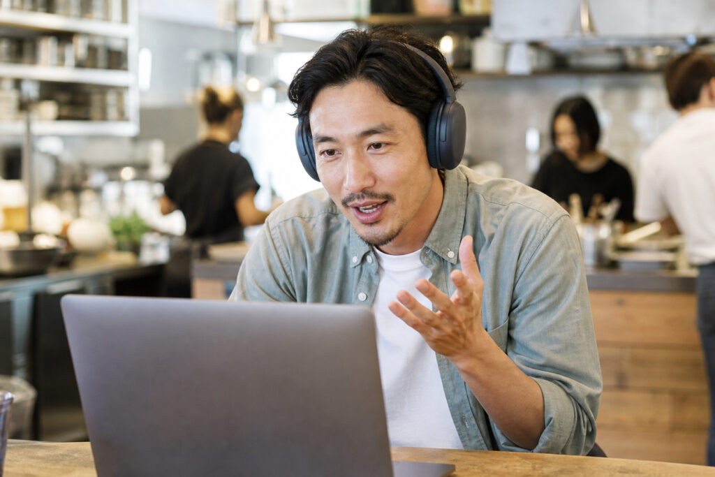 Person taking a video call in a busy cafe wearing boomless wireless headphones